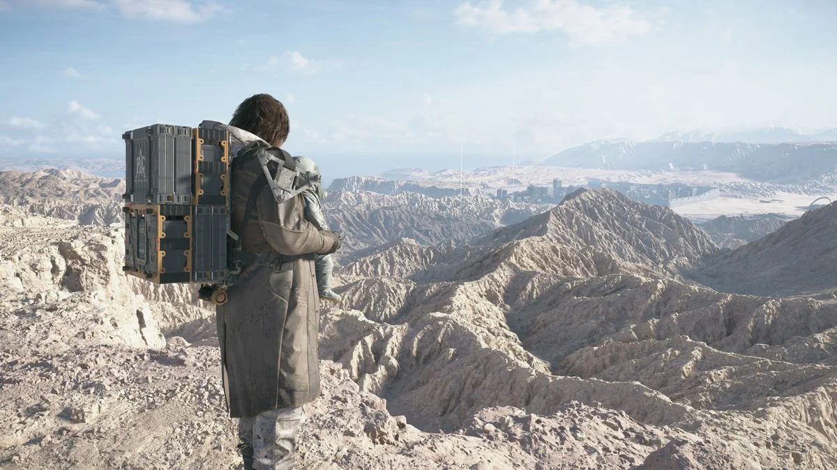 Death Stranding 2 Geburtstag DOOMS: Sam, mit Lou an seiner Brust, steht auf einem Berg und blickt auf ein Wüstental.