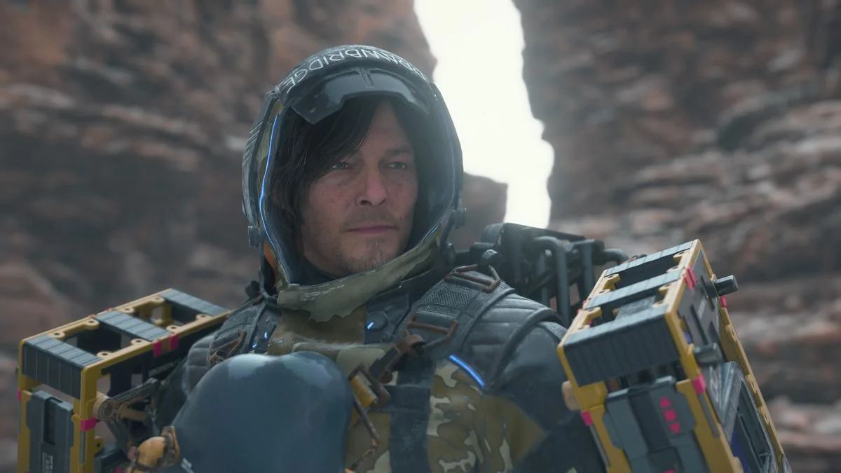 death-stranding-2-erste-eindrucke-und-rezensionen_img_1 | etalongame.de Death Stranding 2 stats: Sam mit Fracht und Mantel, schaut zur Seite, während er in einer Schlucht steht.
