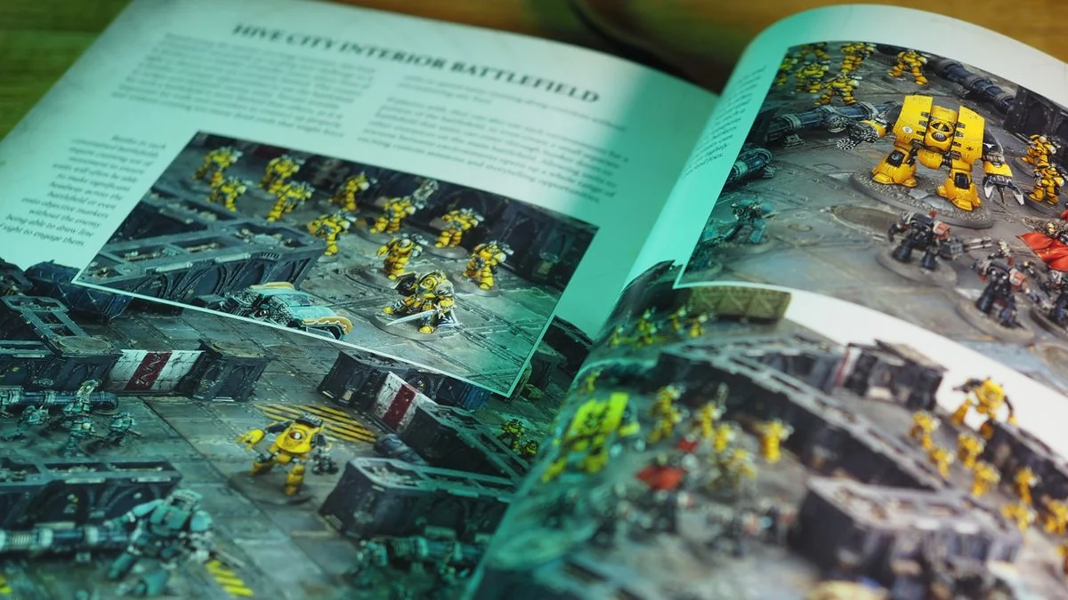 warhammer-the-horus-heresy-saturnine-ein-tiefgehendes-spielerlebnis_img_2 | etalongame.de Das Horus Heresy Kernregelbuch geöffnet auf einer Seite mit Imperial Fists in einer Hive-Umgebung