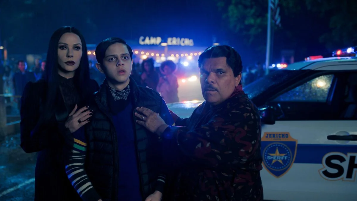 die-besten-neuen-serien-und-filme-eine-wochentliche-ubersicht_img_0 | etalongame.de Catherine Zeta-Jones als Morticia Addams, Isaac Ordonez als Pugsley Addams und Luis Guzmán als Gomez Addams stehen alle in der Nähe eines Polizeiautos in Wednesday Staffel 2.